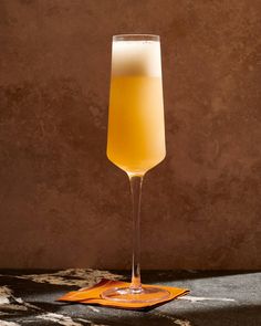 a tall glass filled with liquid sitting on top of a table next to an orange napkin