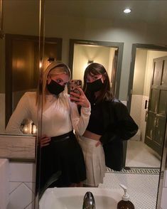 two women wearing face masks are taking a selfie in the bathroom