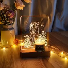 an illuminated lamp with a couple kissing in the middle and some flowers behind it on a wooden table