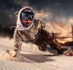 a man riding a snowboard down the side of a snow covered slope at sunset