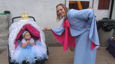 a woman standing next to a baby in a stroller with a princess costume on