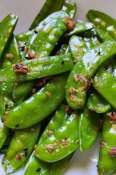 some green beans are sitting on a white plate with brown flecks and seasoning