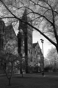 black and white photograph of an old church with trees in the foreground on a cloudy day