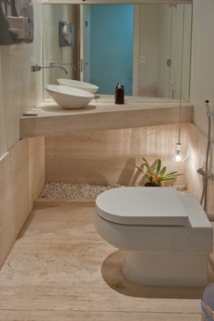 a white toilet sitting in a bathroom next to a sink under a mirror and light