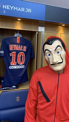 a man in a red hoodie with a fake mask on his face next to a soccer jersey