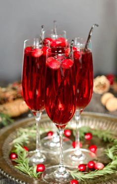 three wine glasses filled with red liquid and garnished with holly wreaths on a platter