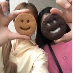 two women are holding up small cookies with faces on them and one has a smiley face