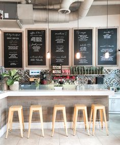 three wooden stools sitting in front of a counter with menus on the wall