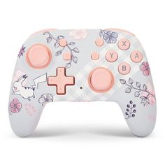 a close up of a controller on a white surface with pink and blue flowers in the background