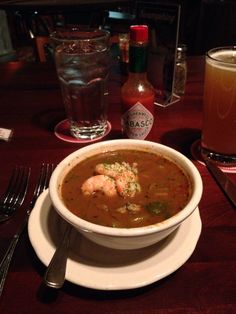 a bowl of soup with shrimp and garnishes on a plate next to a drink