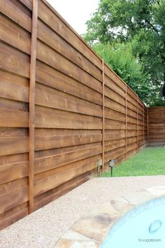 a wooden fence next to a swimming pool in a back yard with grass and trees