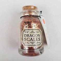 a glass jar filled with lots of red glitter next to a paper tag that says dragon scales