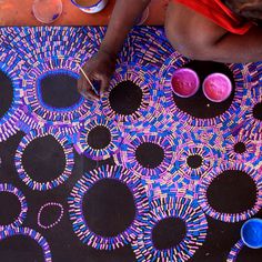 a person sitting on top of a rug with some paint in bowls next to it