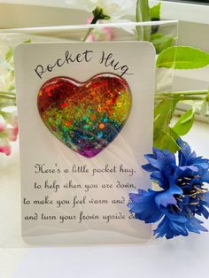 a card with a heart shaped brooch sitting next to a blue flower on a table