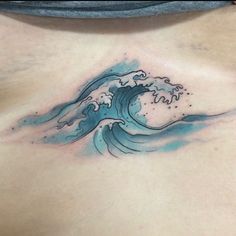 a woman's chest with a blue water wave tattoo on her left side ribcage