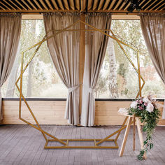 a wedding ceremony setup with flowers and greenery in front of large windows overlooking the forest