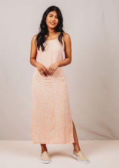 a woman standing in front of a white background wearing an orange and pink floral print dress