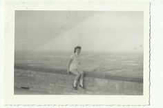 an old black and white photo of a woman sitting on a wall with her legs crossed