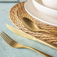 a table setting with silverware and gold utensils on a wicker place mat