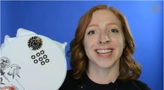 a woman holding up a white plate with black and gold designs on it, in front of a blue background