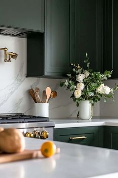 a kitchen with green cabinets and marble counter tops, white flowers in a vase on the stove