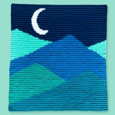 a crocheted blanket with the moon and mountains in blue, green, and white