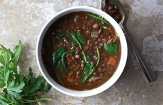 a white bowl filled with beans and greens next to a spoon on top of a table