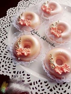 four donuts with pink frosting and bows are on a white doily plate