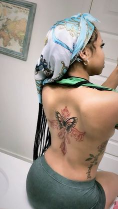 a woman with a scarf on her head is sitting on the toilet and has tattoos on her back