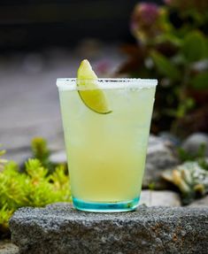 a lemonade drink with a lime wedge on the rim sits on a rock in front of some plants