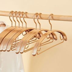 clothes hangers are hanging on a wooden rail in front of a white shirt and beige wall