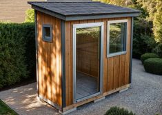 a small wooden building in the middle of a garden with gravel and bushes around it