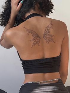 a woman with a butterfly tattoo on her back is looking into the distance while she brushes her hair