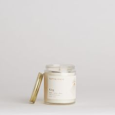 a candle with a gold lid next to it on a white surface, the candle is empty