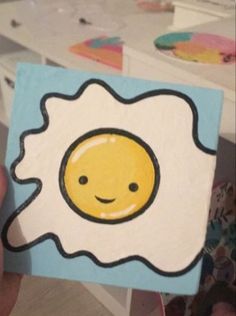 a hand holding up a painted egg with a smiley face on it's side