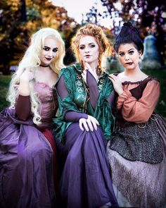 three women dressed up as witches sitting next to each other on a bench in the grass