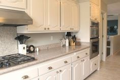 a kitchen with white cabinets and marble counter tops, along with a stove top oven