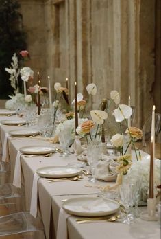 a long table is set with white and gold place settings, candles, and flowers