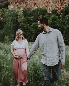 a pregnant couple walking through the grass holding hands