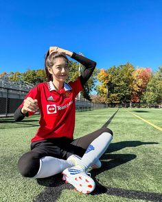 a woman sitting on top of a soccer field holding her hair in one hand and smiling at the camera