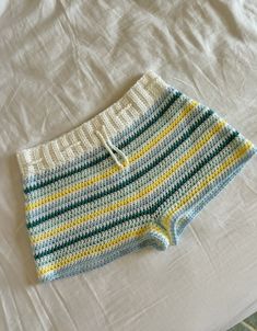 a crocheted shorts laying on top of a white bed next to a pillow