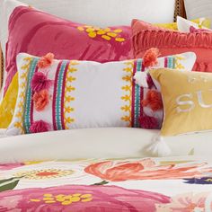 a bed topped with lots of pillows next to a white headboard covered in pink and yellow flowers