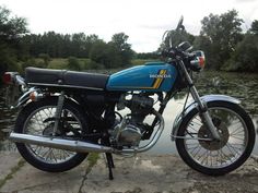 a blue and black motorcycle parked next to a body of water with trees in the background