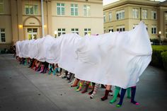 a line of people wearing colorful rain boots and covering them with white sheet in front of a building