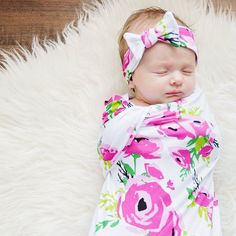 a baby wrapped in a pink flowered wrap sleeping on top of a fluffy white rug