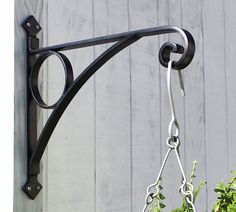 a black metal hook on the side of a building with green plants hanging from it