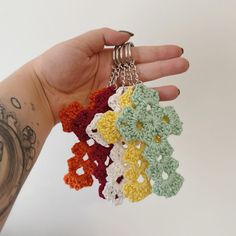 a hand holding four crocheted keychains in different colors and designs on it