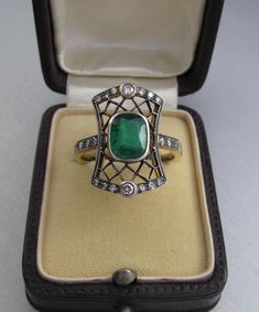 Art Deco emerald ring with diamonds, made of 14K gold and silver. With a Hungarian 14K hallmark that was used after 2016. The top part is made of silver. The head part of the ring is 0.796 inches (20 mm) long. Gemstone: one piece of emerald, 1.54 carat, its size is: 0.24 inches * 0.31 inches (6.1 mm * 7.8 mm) The emerald has inclusions which unfortunately affects the surface of the stone as well. I tried to make photos of that. Additional gemstone details: 20 single cut diamonds Carat weight: 0. Art Deco Emerald Ring With Rose Cut Diamonds, Art Deco Green Emerald Ring With Rose Cut Diamonds, Elegant 14k Stamped Emerald Ring, Antique Emerald Cut Yellow Gold Emerald Ring, Art Deco Emerald Diamond Ring With Accents, Antique Emerald Cut Emerald Ring, Antique Green Oval Diamond Ring, Antique Green Ring With 17 Jewels, Formal Emerald Ring With Intricate Design