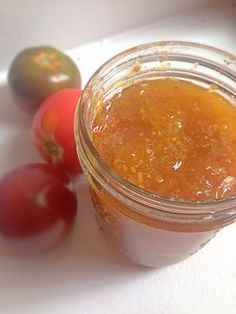 a jar filled with food sitting next to some tomatoes on a white counter top and another tomato in the background