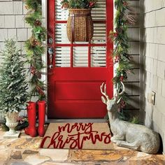 a red front door decorated for christmas with evergreen garland and deer statue next to it